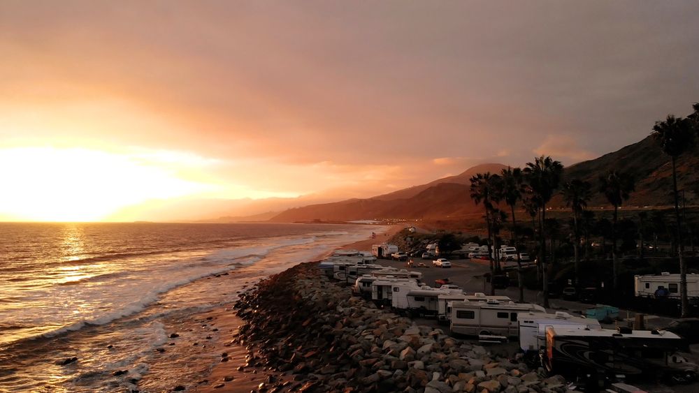 RVs parked by the water with a sunset